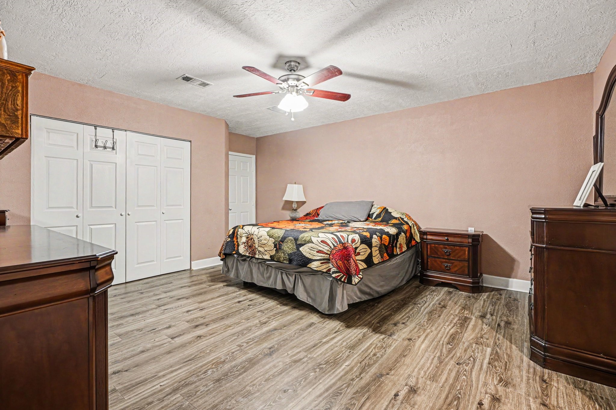 5104 Avenue R Santa Fe, TX 77510 - Photo 18 of 35 This spacious bedroom features warm-toned walls, wood flooring, and a ceiling fan. It includes ample storage with multiple closets and a cozy setup.