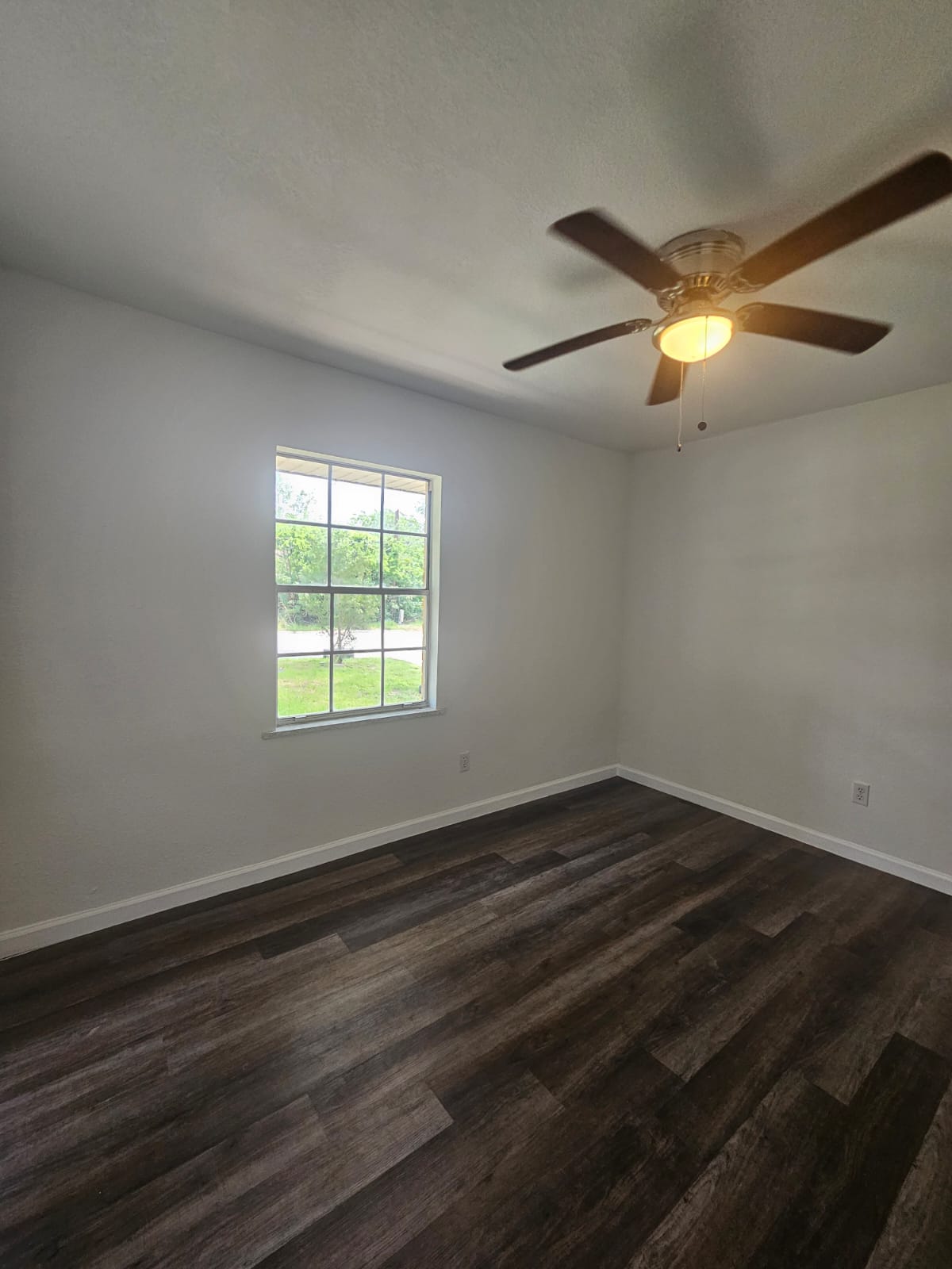 1401 Trinity Street Lockhart, TX 78644 - Photo 12 of 31 Room featuring a window with exterior views, dark wood-finish flooring, white baseboards, and a ceiling fan with integrated lighting