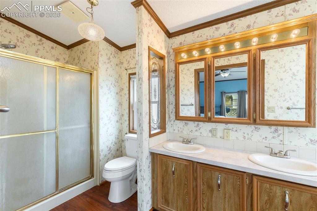 13335 Gymkhana Road Peyton, CO 80831 - Photo 29 of 38 Bathroom featuring a dual vanity with oak-finish cabinetry, a shower with a gold-tone framed sliding glass door, a water closet, and wood-finish flooring
