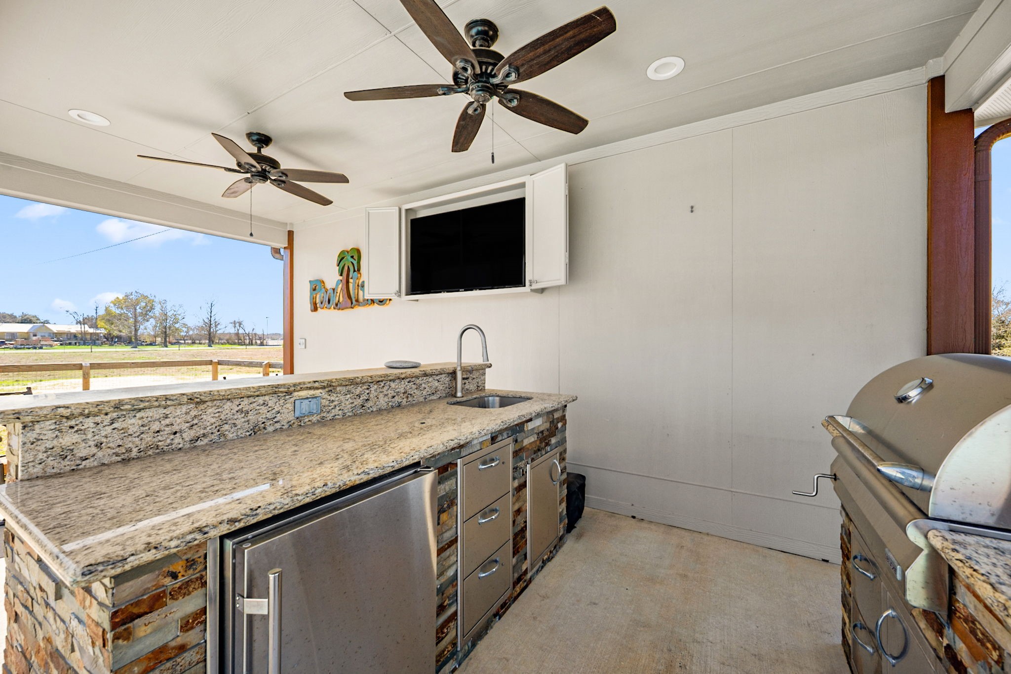 26253 Sharp Road Katy, TX 77493 - Photo 19 of 25 Take entertaining to the next level with this fully equipped outdoor kitchen—featuring built-in grill, sink, refrigerator, generous prep space, ceiling fans, and mounted TV—perfect for game days, cookouts, and relaxed gatherings just steps from the pool and patio.
