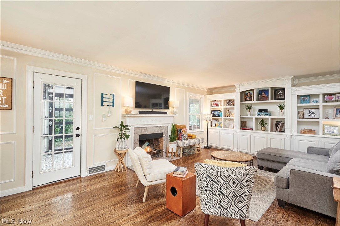 183 Overwood Road Akron, OH 44313 - Photo 7 of 34 Living area featuring wood-finish flooring, a white fireplace with a stone surround, an integrated television mount, a white paneled door with glass inserts, and extensive built-in white cabinetry with shelving