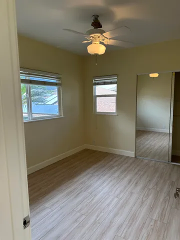 an empty room with wooden floor chandelier fan and windows
