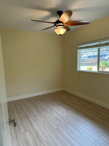 an empty room with wooden floor fan and windows