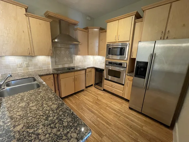 a kitchen with stainless steel appliances granite countertop a refrigerator a stove and a sink with wooden floor