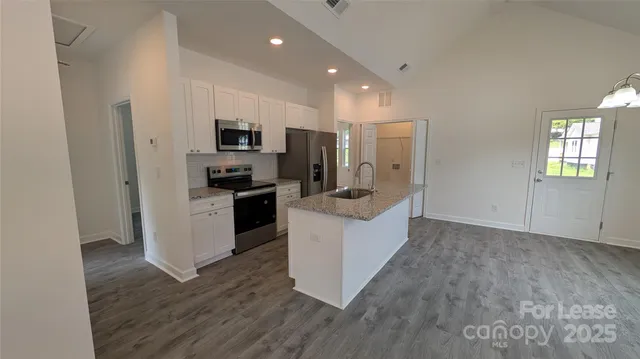 a kitchen with stainless steel appliances granite countertop a refrigerator a stove and a sink with wooden floor