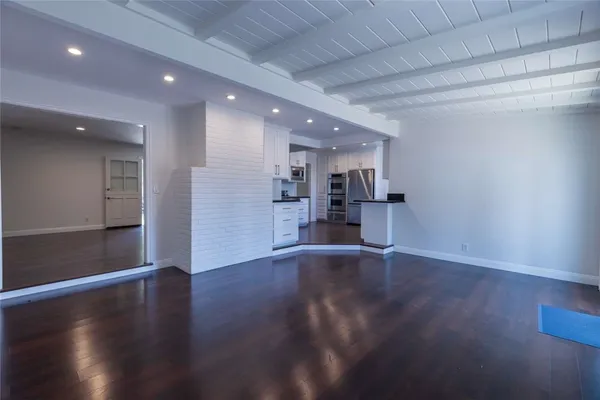a view of empty room with wooden floor and kitchen