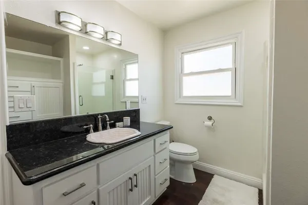 a bathroom with a granite countertop sink a large mirror a toilet and a window