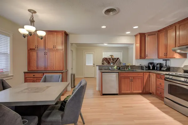 a kitchen with stainless steel appliances kitchen island granite countertop a stove a sink a refrigerator and a dining table with wooden floor