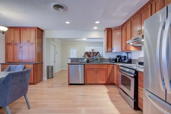 a kitchen with stainless steel appliances granite countertop a refrigerator a sink dishwasher and wooden cabinets with wooden floor