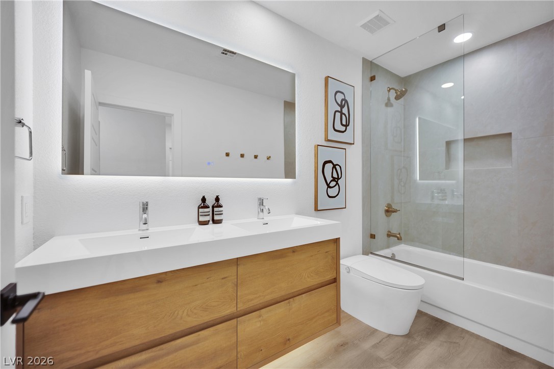 8981 Rivers Edge Drive Las Vegas, NV 89117 - Photo 30 of 69 Modern bath with dual sinks, warm wood cabinetry, and a sleek glass-enclosed shower over tub.
