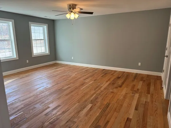 an empty room with wooden floor chandelier fan and windows