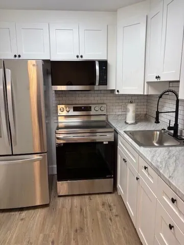 a kitchen with granite countertop a refrigerator stove and white cabinets