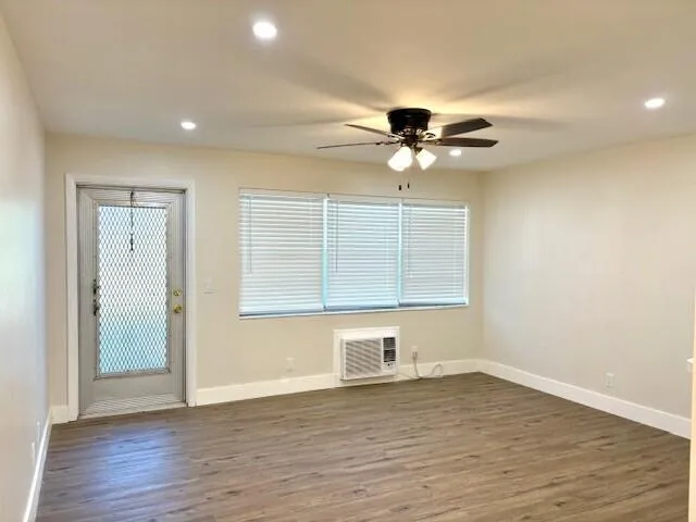 a view of an empty room with wooden floor and a ceiling fan