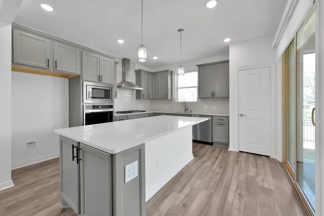 a large kitchen with a center island wooden floor stainless steel appliances and windows