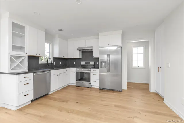 a kitchen with granite countertop a refrigerator oven a sink dishwasher and white cabinets with wooden floor