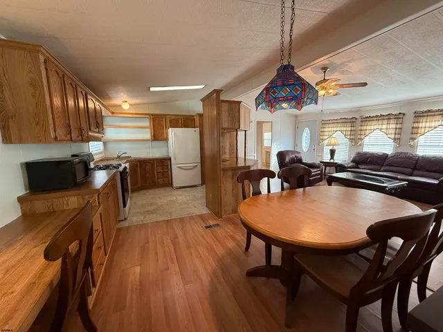 a dining hall with stainless steel appliances granite countertop a stove a refrigerator a kitchen island a dining table and chairs with wooden floor