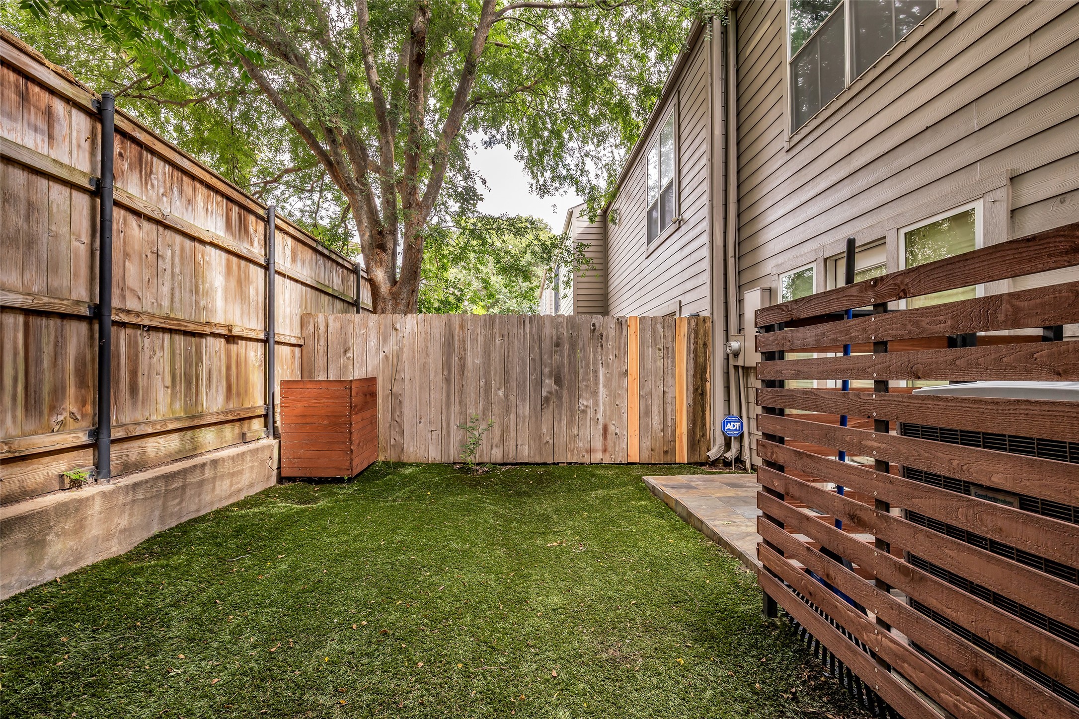 7485 Brompton Street, Unit 7485 Houston, TX 77025 - Photo 37 of 43 This outdoor space features a private, fenced yard with artificial turf for easy maintenance. It's bordered by a tall wooden fence and shaded by a large tree, offering a cozy and secluded area for relaxation or small gatherings.