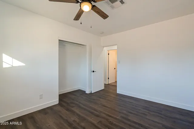 an empty room with wooden floor fan and windows