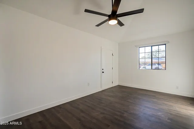 an empty room with wooden floor ceiling fan and windows