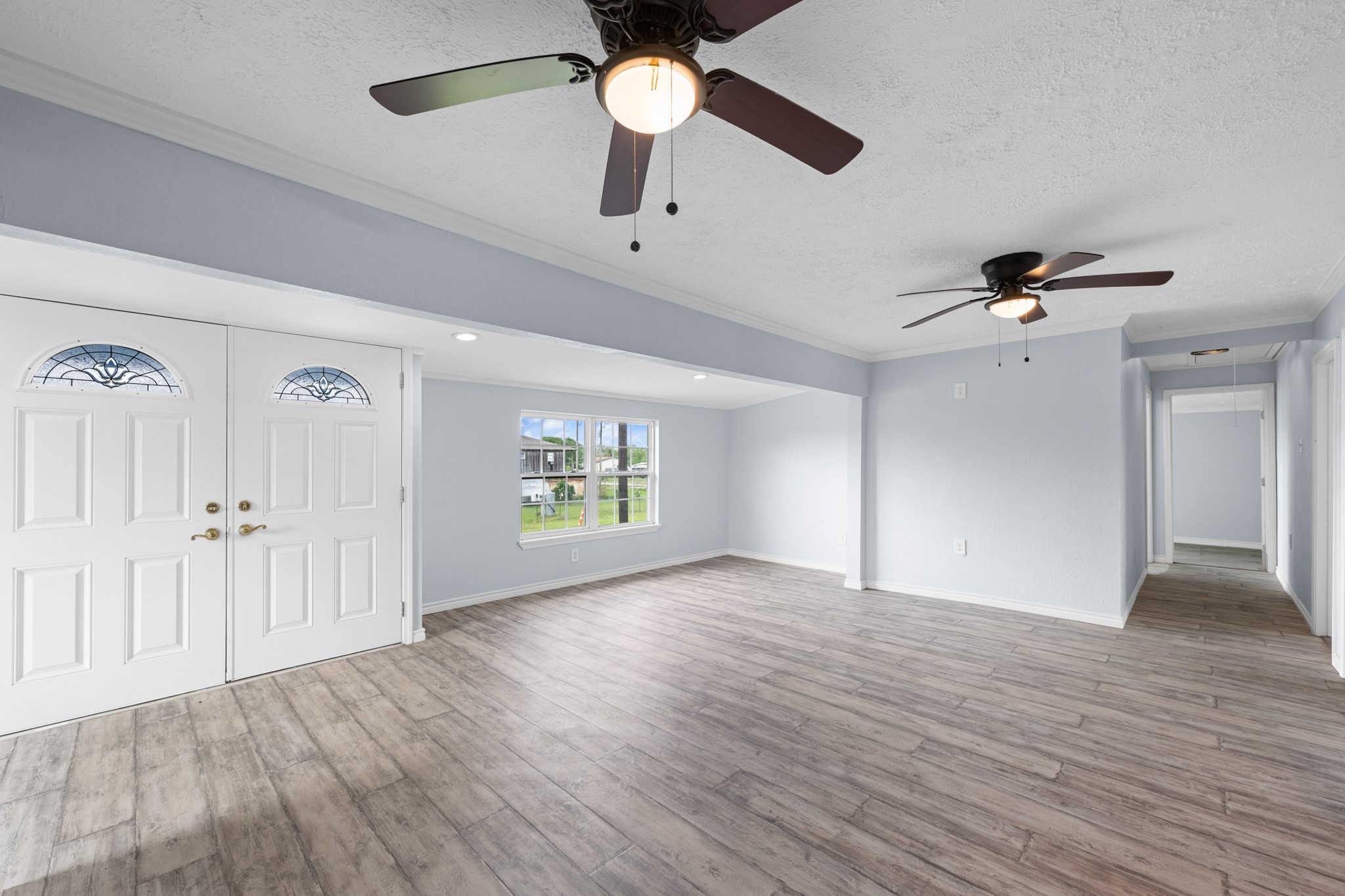 2534 Bastrop Angleton, TX 77515 - Photo 5 of 50 Bright and spacious living area featuring updated wood-look flooring, soft neutral tones, and multiple ceiling fans for added comfort. The open layout and large windows create an inviting atmosphere with plenty of natural light throughout.