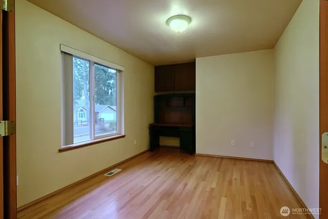 an empty room with wooden floor closet and windows