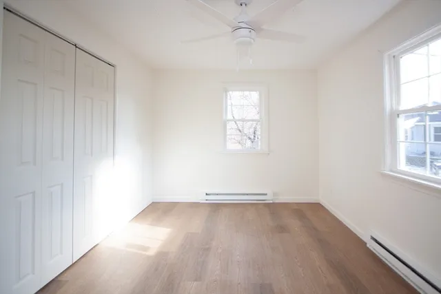 an empty room with wooden floor chandelier fan and windows