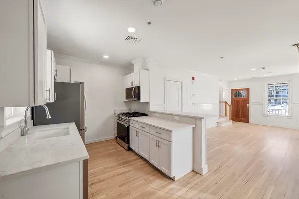 a kitchen with stainless steel appliances granite countertop a stove top oven a sink a refrigerator white cabinets and wooden floor