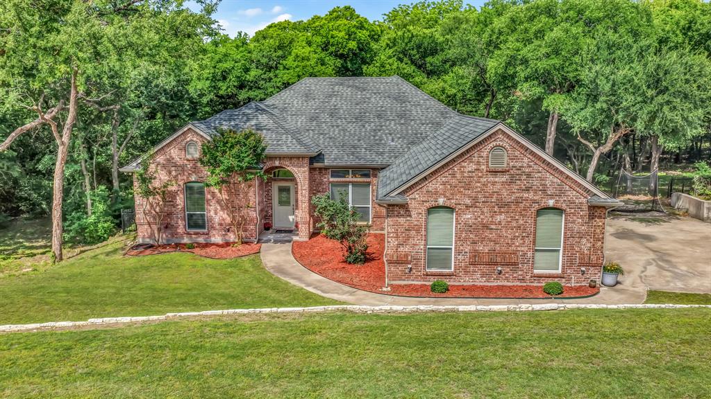 203 Mockingbird Lane Aledo, TX 76008 - Photo 2 of 37 Brick exterior residence featuring an arched entry, a shingled roof, a concrete driveway, and established trees framing the property