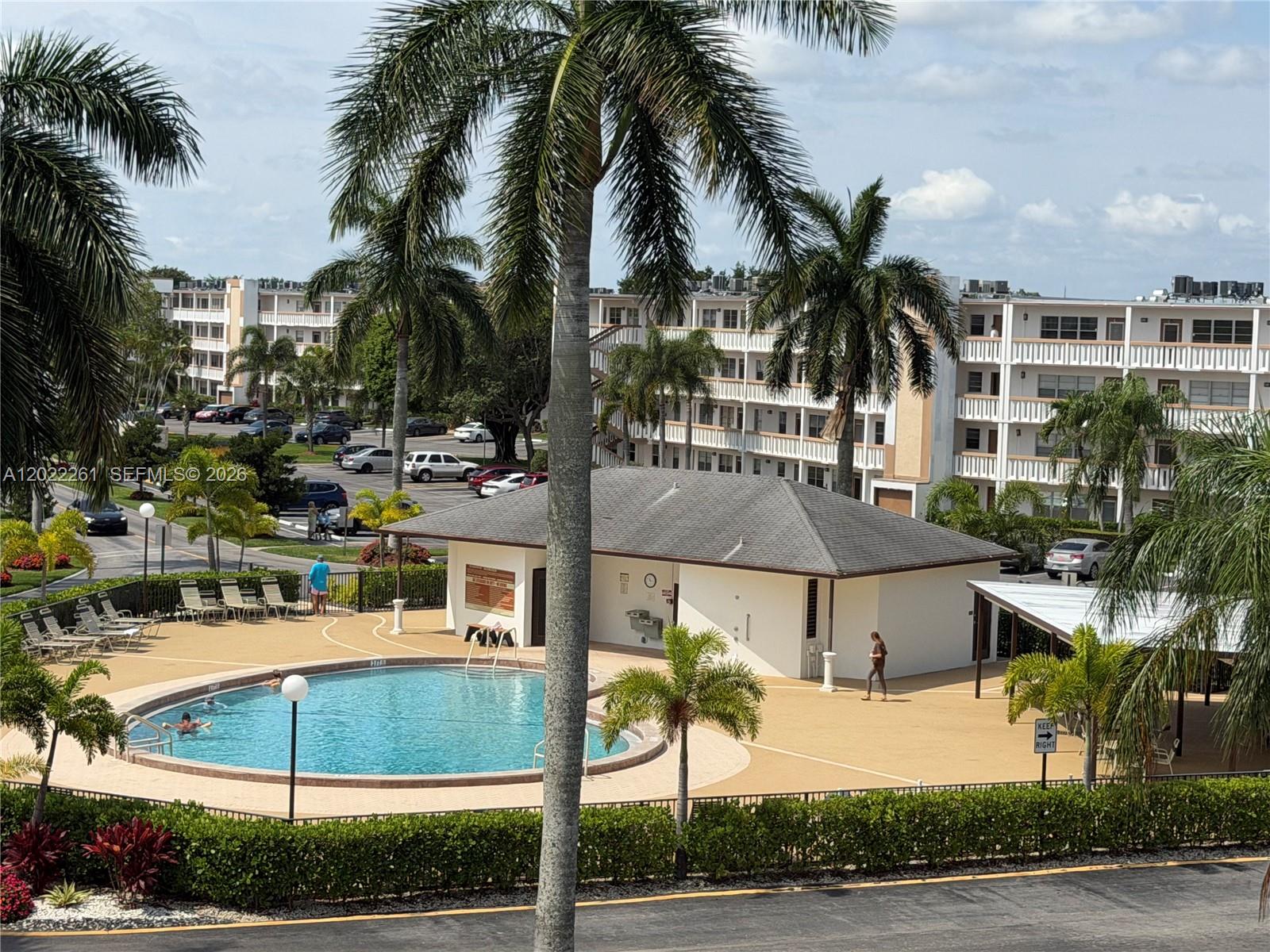 4043 Cornwall C, Unit 4043 Boca Raton, FL 33434 - Photo 14 of 16 a view of a white house with a yard and table and chairs under palm trees