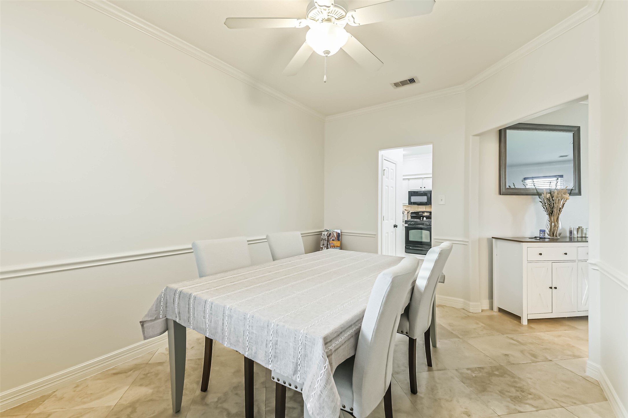 22538 Goss Spring Court Spring, TX 77373 - Photo 16 of 36 This dining area features a neutral color palette with a ceiling fan, a table that seats six, and tiled flooring. An adjoining doorway leads to the kitchen, and there's a small sideboard with decor, enhancing functionality and style.