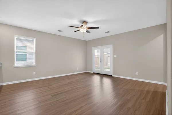 an empty room with wooden floor ceiling fan and windows