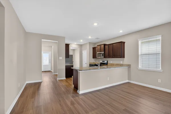 a large living room with stainless steel appliances granite countertop a stove top oven a sink dishwasher and a refrigerator with wooden floor