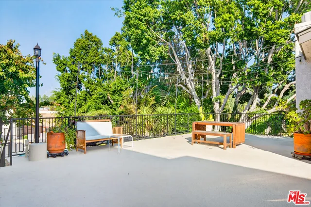 a wooden bench sitting in backside of a house with large trees and lawn chairs