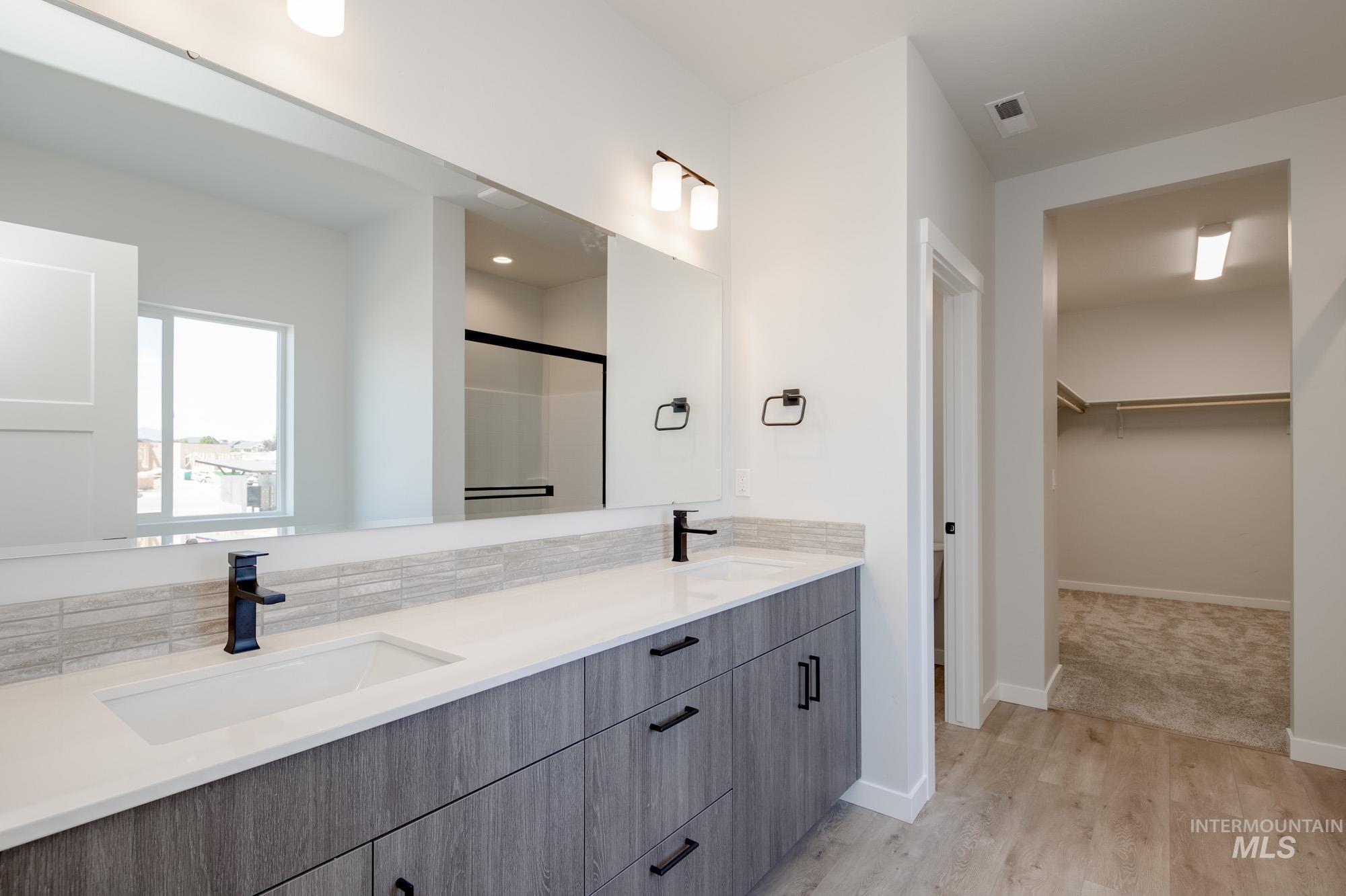 6596 South Banded Eagle Way Boise, ID 83709 - Photo 21 of 28 Bathroom with double vanity, a walk in closet, wood finished floors, decorative backsplash, and a shower with door