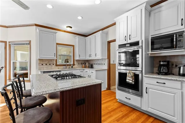 a kitchen with stainless steel appliances granite countertop a stove top oven a sink dishwasher and white cabinets with wooden floor