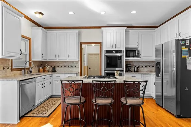 a kitchen with stainless steel appliances kitchen island granite countertop a table chairs microwave and sink
