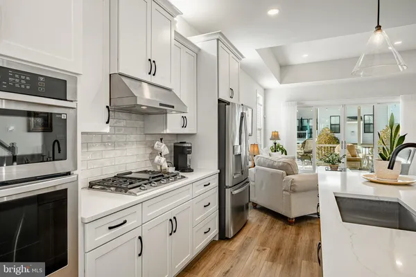 a kitchen with stainless steel appliances kitchen island granite countertop a refrigerator a stove a sink dishwasher and white cabinets with wooden floor