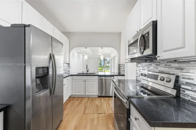 a kitchen with stainless steel appliances granite countertop a refrigerator a stove and a sink with wooden floor