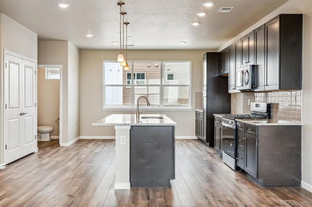 a kitchen with stainless steel appliances granite countertop a refrigerator a stove top oven a sink dishwasher and a refrigerator with wooden floor