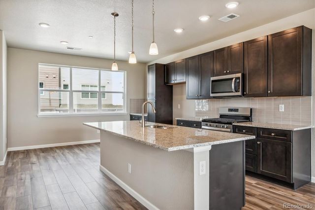 a large kitchen with granite countertop a stove a sink a center island and wooden floor