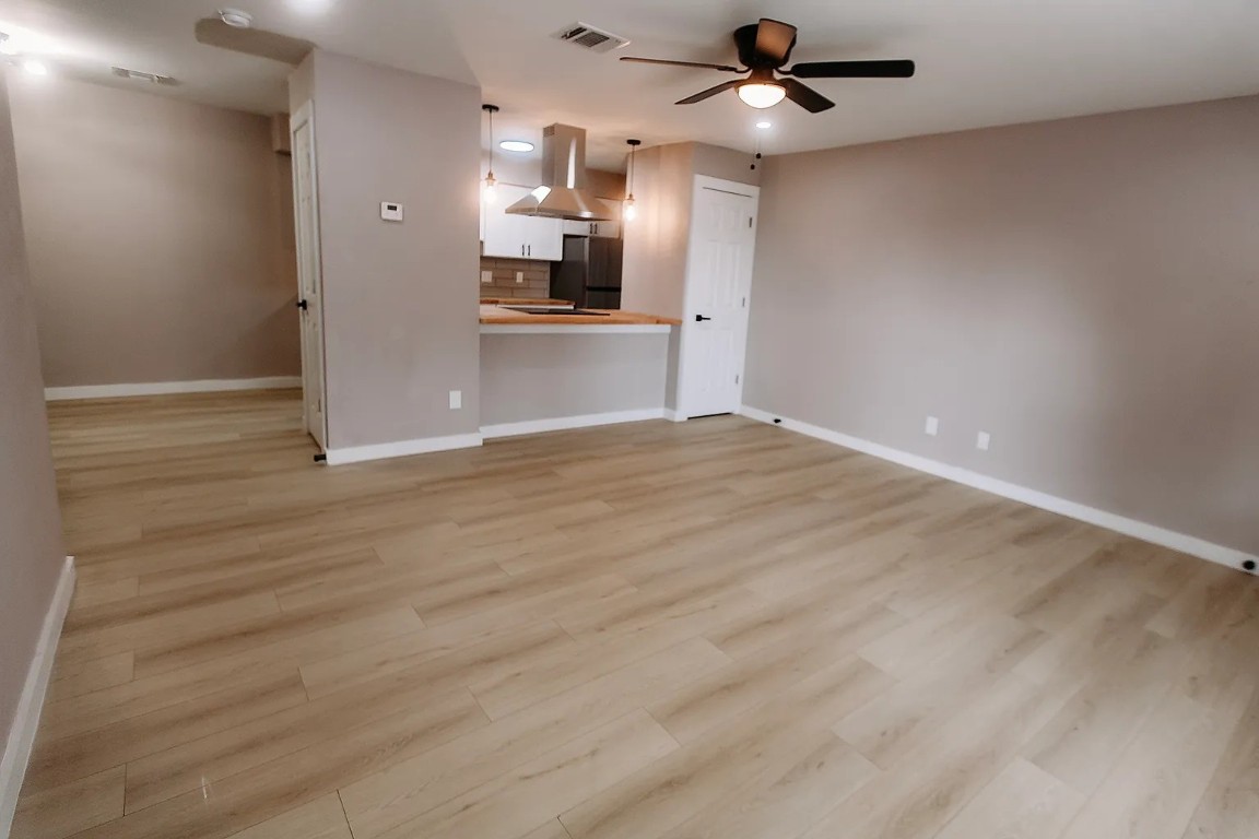 an empty room with wooden floor kitchen view and a ceiling fan