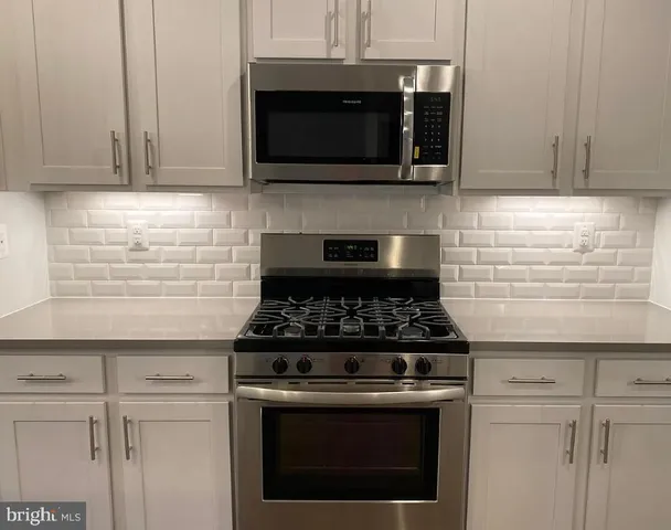 a kitchen with stainless steel appliances granite countertop white cabinets and a stove top oven