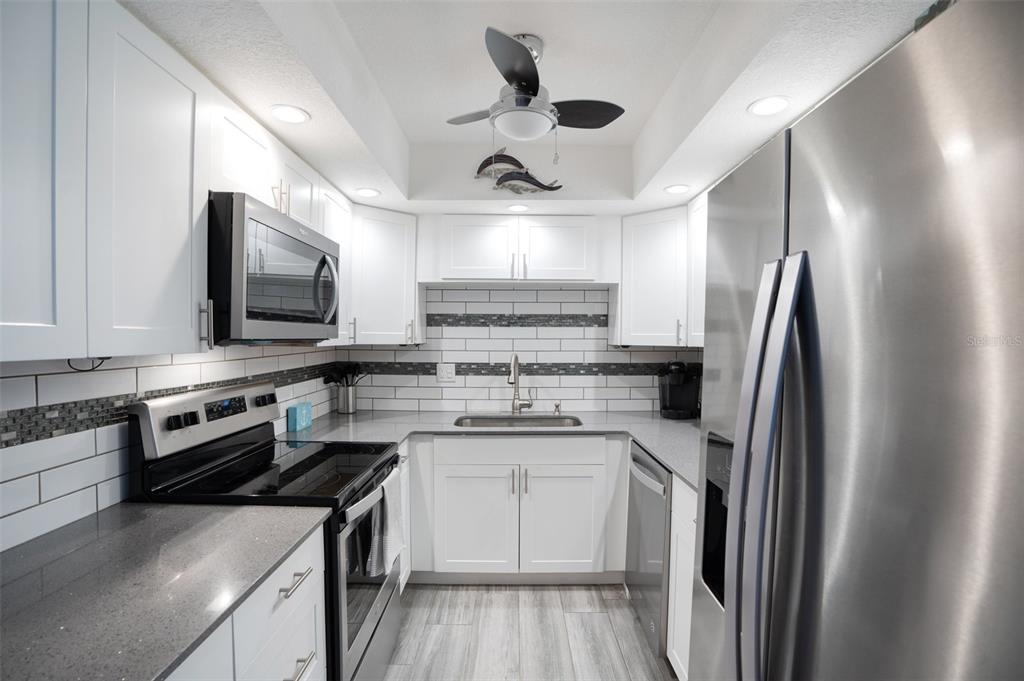 5855 Midnight Pass Road, Unit 327 Sarasota, FL 34242 - Photo 7 of 47 a kitchen with stainless steel appliances granite countertop a sink stove a refrigerator and white cabinets with wooden floor