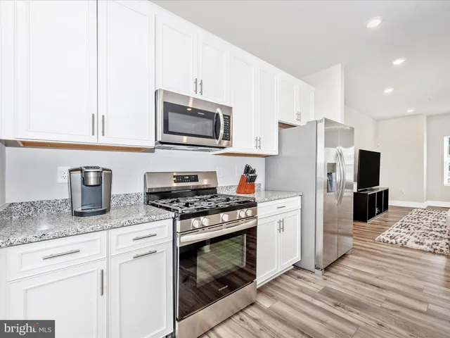a kitchen with stainless steel appliances granite countertop a stove top oven a sink a refrigerator white cabinets and wooden floor next to a window
