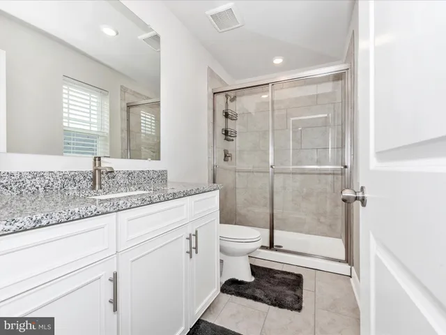 a bathroom with a granite countertop sink a toilet a mirror and shower