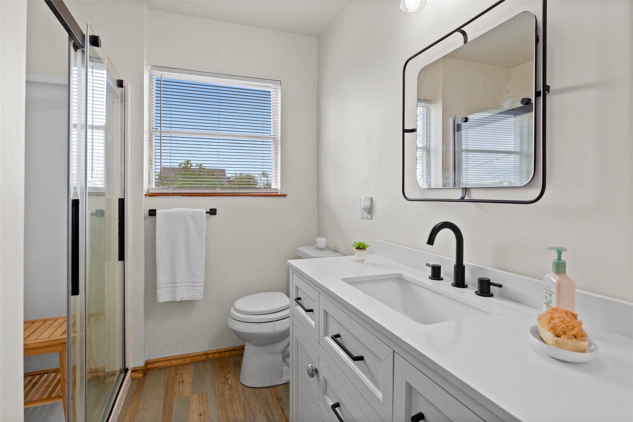 1619 FM 517 Road East San Leon, TX 77539 - Photo 17 of 27 This bathroom features a modern design with a sleek vanity, black fixtures, and a large mirror. It includes a glass-enclosed shower, a window for natural light, and light wood flooring, creating a bright and inviting space.