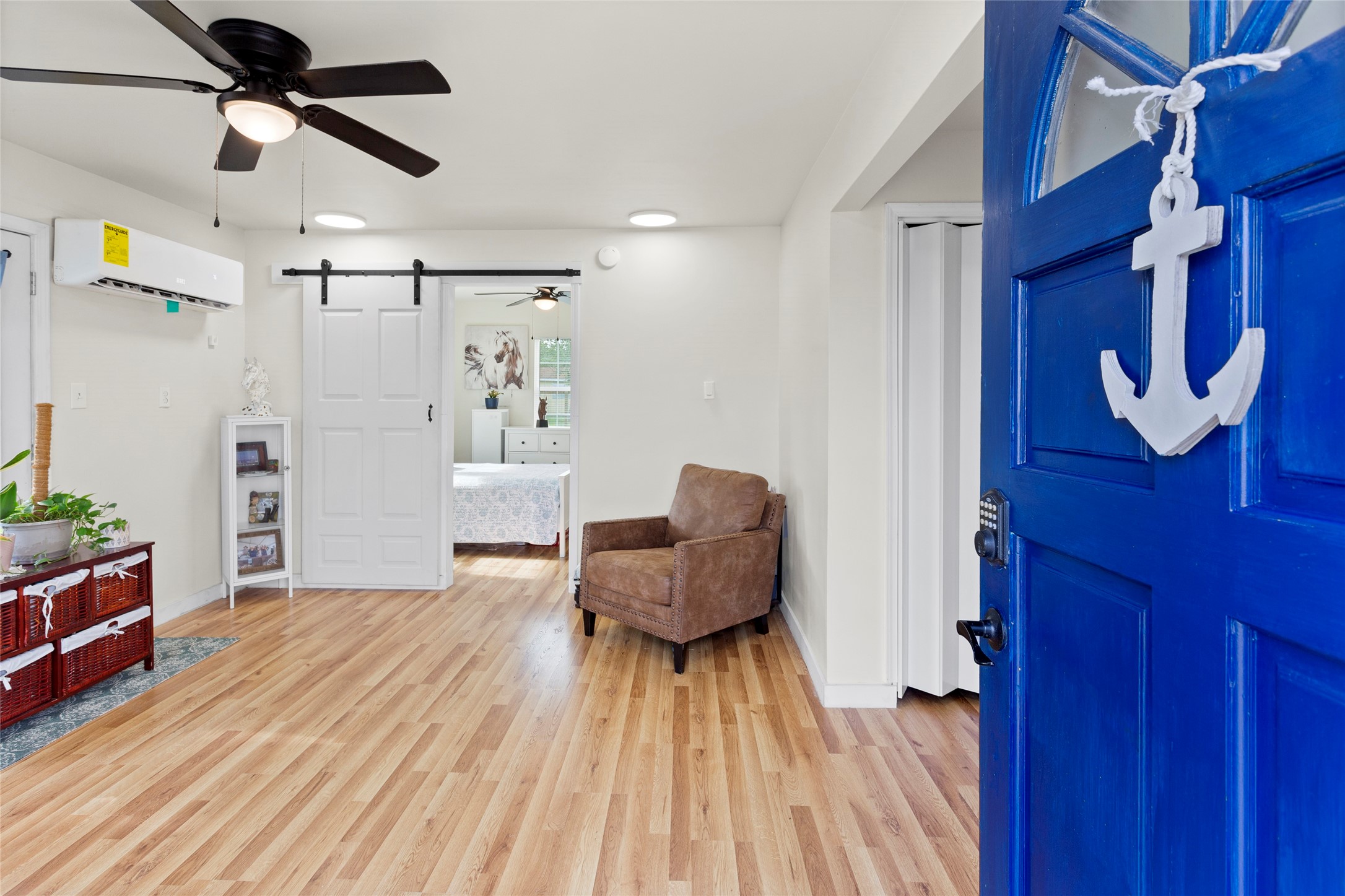 1619 FM 517 Road East San Leon, TX 77539 - Photo 3 of 27 This inviting entryway features a bright blue door leading into a cozy room with light luxury vinyl floors. Modern ceiling fan and a sliding barn door that opens to a glimpse of a the primary bedroom.