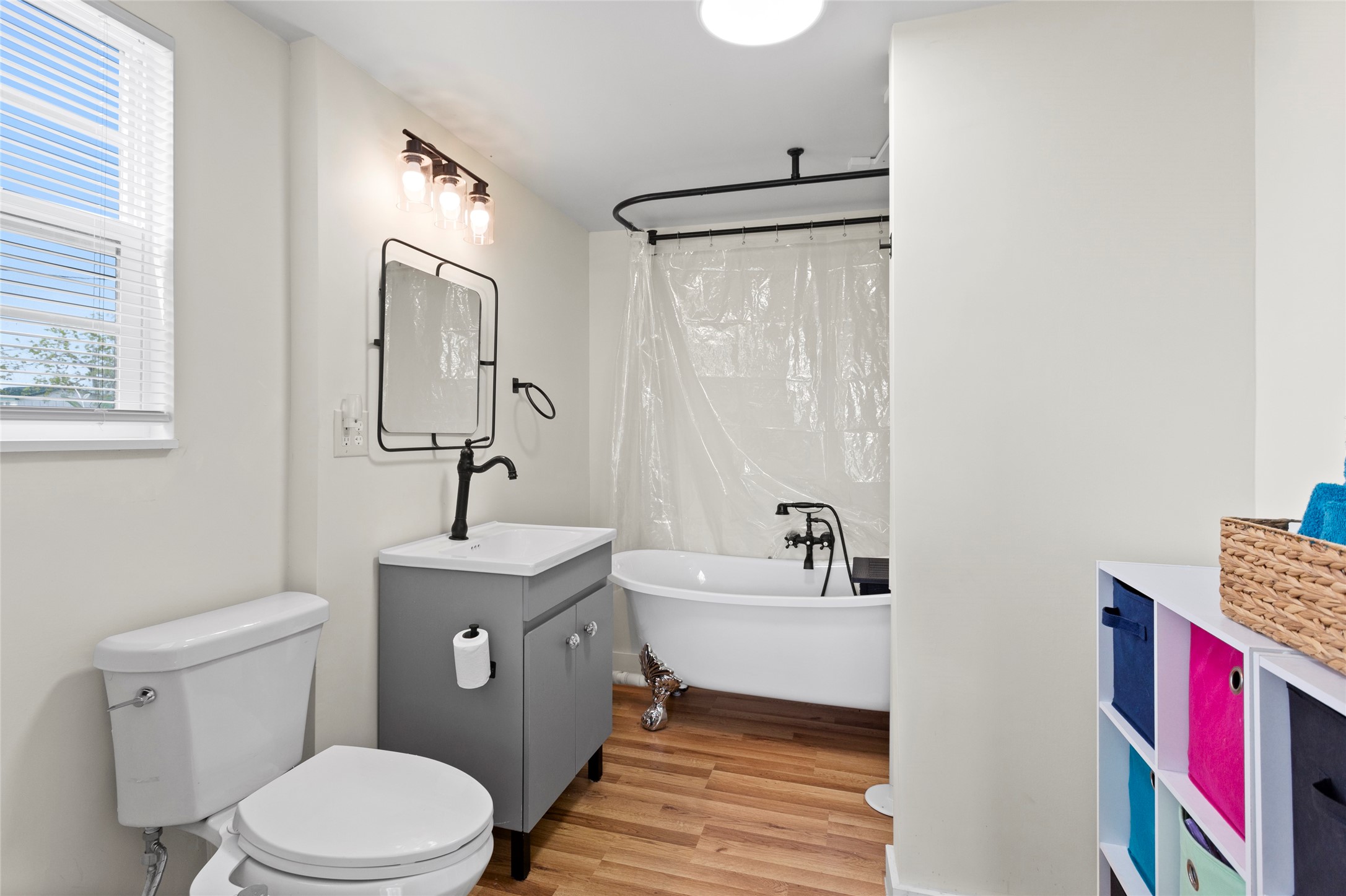 1619 FM 517 Road East San Leon, TX 77539 - Photo 7 of 27 This bathroom features a modern design with a freestanding clawfoot tub, sleek black fixtures, and a stylish vanity. The space is bright with natural light from a window, complemented by the warm luxury vinyl flooring.