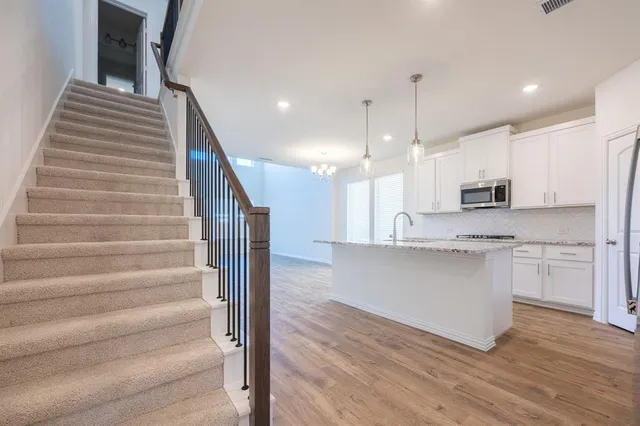 a kitchen with stainless steel appliances granite countertop a sink a stove a refrigerator and white cabinets with wooden floor