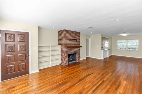 a view of an empty room with wooden floor fireplace and a window